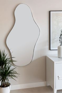 a mirror sitting on top of a white dresser next to a potted plant