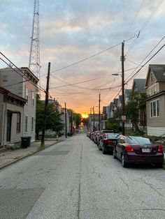 cars are parked on the street in front of houses and telephone poles as the sun sets