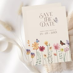 an image of save the date card with flowers and butterflies on it next to feathers