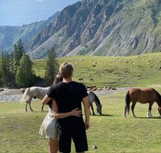 a man and woman standing in front of horses on a field with mountains in the background