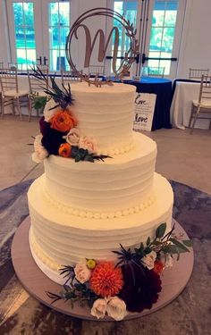 a three tiered white cake with flowers on the side and monogram above it