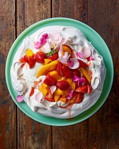 a cake with white frosting and fruit toppings on a green plate next to a wooden table