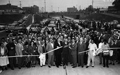 a large group of people standing in front of a line of cars with a ribbon