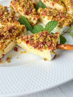 several pieces of dessert on a white plate with mint leaves and sprinkles