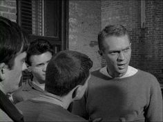 three men talking to each other in front of a brick building