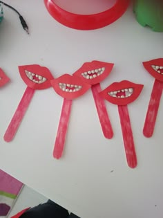 some red paper sticks with mouths and teeth on top of a white table next to a cup