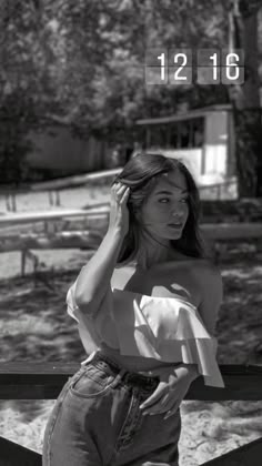 a woman leaning on a fence with her hand in her hair and looking off to the side