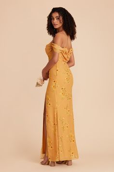 a woman wearing an off the shoulder yellow dress with floral print on it and side slit