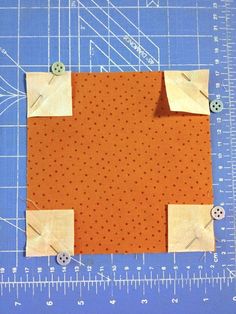 an orange piece of fabric with holes cut into it and some sewing needles next to it