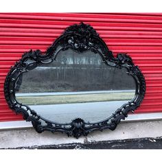 an ornate black mirror sitting on the side of a building next to a red wall