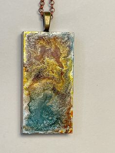 a square pendant with an abstract painting on it's side hanging from a chain