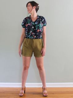 a woman standing in front of a wall wearing high heeled sandals and a floral shirt