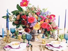 a table topped with lots of colorful flowers and place settings on top of a wooden table