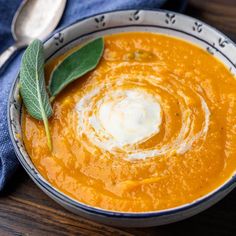 a bowl filled with carrot soup on top of a wooden table next to a spoon