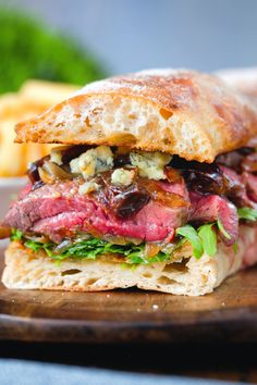 a roast beef sandwich with lettuce, tomato and other toppings on a wooden cutting board