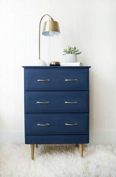 a blue dresser sitting on top of a white rug next to a lamp and potted plant