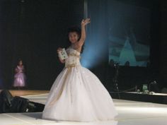 a woman in a white dress standing on top of a stage with her arms up