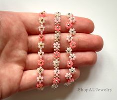 a hand is holding four bracelets with pink and white flowers on them, each beaded in different colors