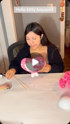 a woman sitting at a table with pink flowers in front of her and an object on top of the table