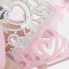 a close up of a person holding a pink tiara with hearts and jewels on it