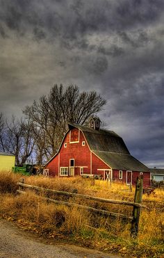 an old red barn sits in the middle of a grassy field under a cloudy sky