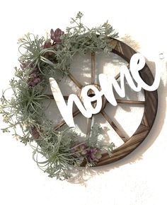 a wooden wheel with the word home spelled in white letters surrounded by flowers and greenery