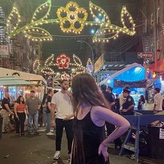 a woman standing in the middle of a crowded street at night with lights strung overhead