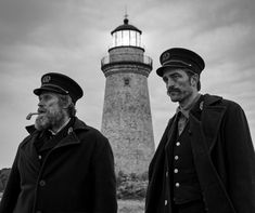 two men standing next to each other in front of a lighthouse