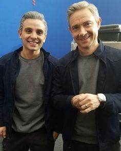 two men standing next to each other in front of a blue wall