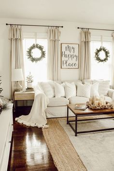 a living room filled with white furniture and christmas wreaths on the window sill