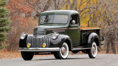 an old truck is parked on the side of the road in front of some trees