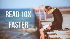 a young man sitting on top of a cement wall next to the ocean reading a book