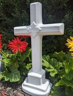 a white cross sitting in the middle of some flowers