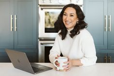 a woman sitting at a kitchen table with a laptop and coffee mug in front of her