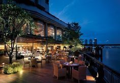 an outdoor dining area with tables and chairs next to the water at night in front of a restaurant