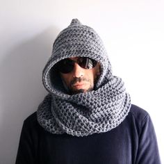 a man wearing sunglasses and a crocheted scarf around his neck is standing in front of a white wall