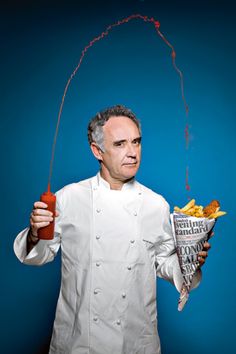 a man holding a hot dog and ketchup in his hand while wearing a chef's coat