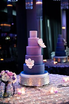 a purple and blue wedding cake sitting on top of a table with candles in front of it