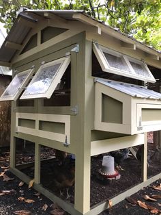 a chicken coop with two windows on the roof and one in the ground, next to a tree