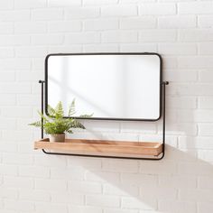 a white brick wall with a black metal frame mirror and wooden shelf holding a potted plant