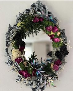 a mirror that has flowers on it and plants in the frame around it, hanging on a wall