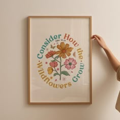 a woman is holding up a framed poster with flowers on it that reads, consider how many wildflowers grow