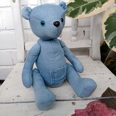 a blue teddy bear sitting on top of a white bench next to a plant and potted plant