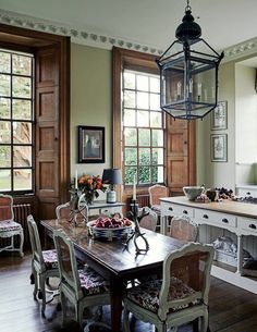 a dining room table and chairs in front of two large windows with wooden trimmings