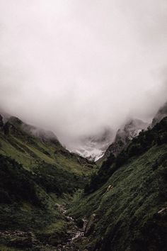 the mountains are covered in clouds and green grass, with a stream running between them