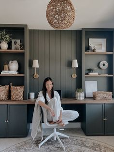 a woman sitting on a chair in front of a desk with bookshelves and baskets