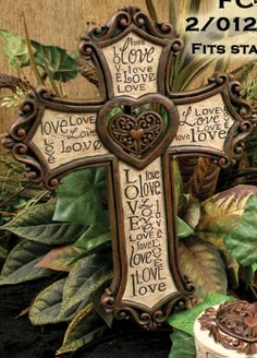 a wooden cross sitting on top of a table next to flowers and greenery in front of a wall