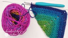 a crochet triangle next to a ball of yarn with a knitting needle on it