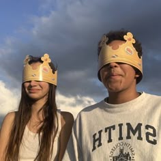 two people with crowns on their heads standing next to each other in front of a cloudy sky