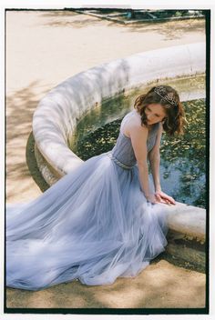 a woman in a blue dress leaning on a fountain